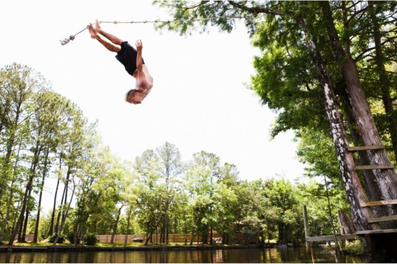 A man back flips off a rope swing into a water.