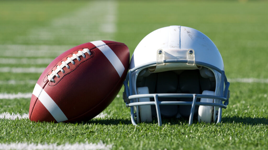 A football and helmet at an NFL stadium field.