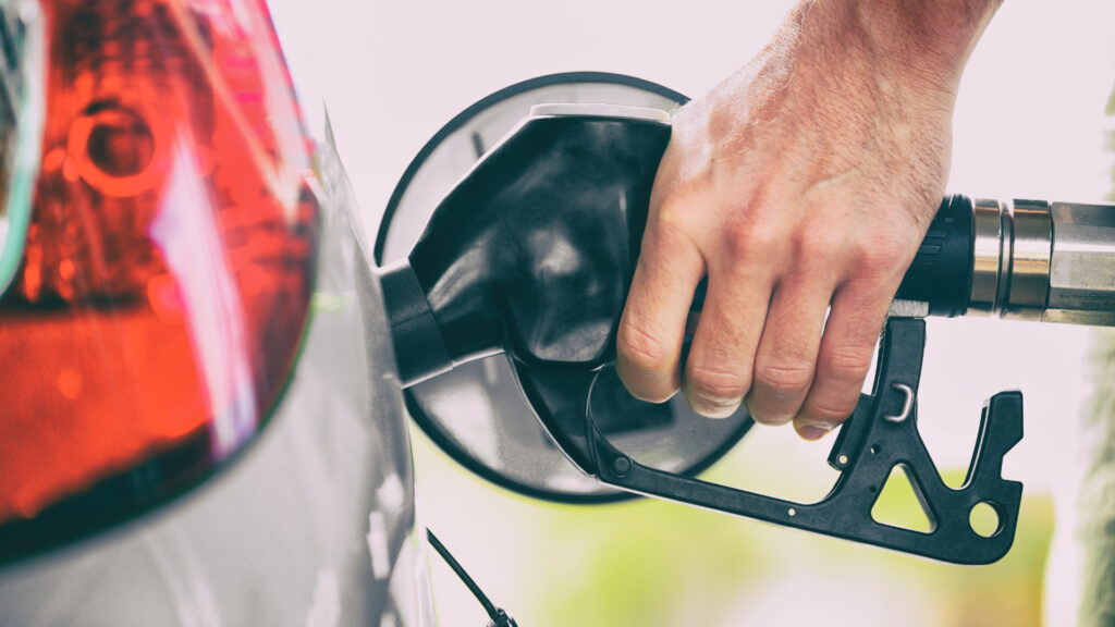 Close up of a hand of a person pumping gas while their car is running.