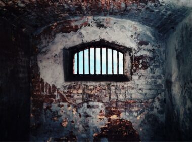 Inside a deteriorated brick prison looking out the barred window.