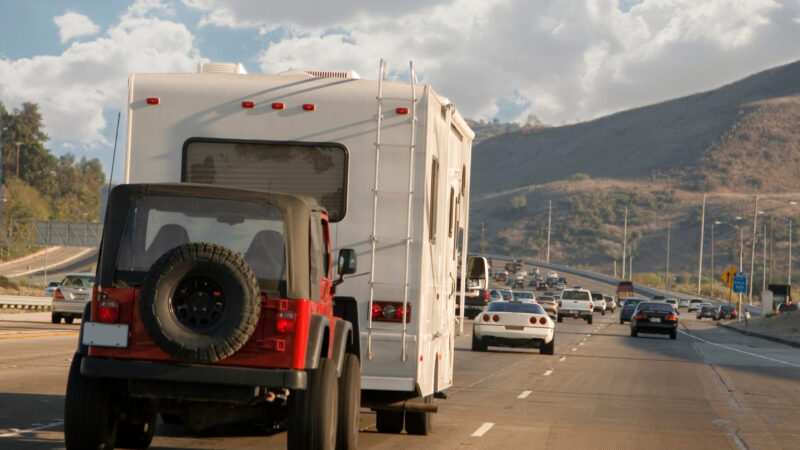 An RV towing a jeep on a busy road.