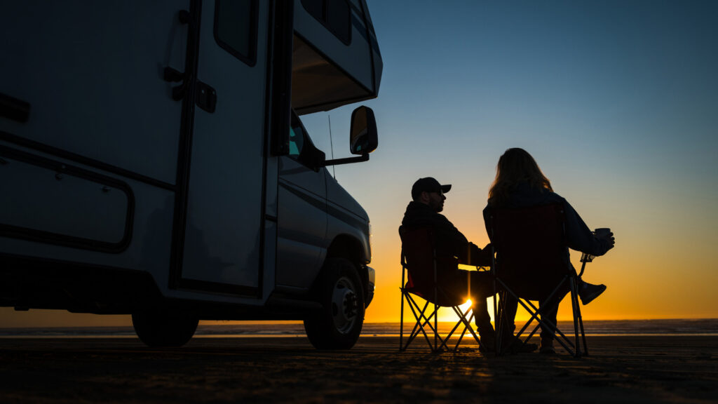A couple sitting in chairs outside of their RV enjoying the sunset.