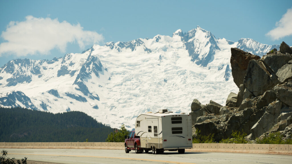 An RV being towed by a trailer on the highway in Alaska.