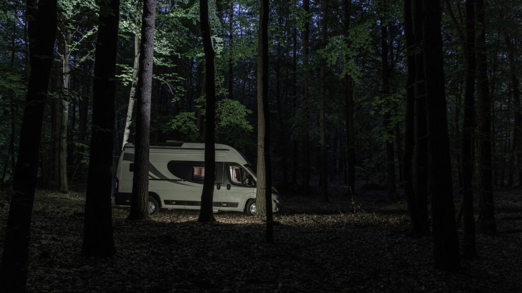 An RV parked in the woods at night.