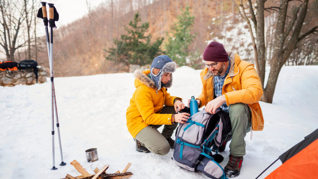 A father and his son grabbing camping gear out of their bags in the winter.