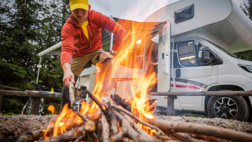 A man working on a campfire outside of his camper van.