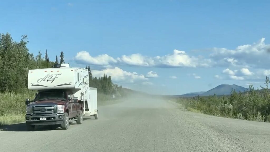 An RV with a truck camper pulled off on the side of the Alaska Highway.