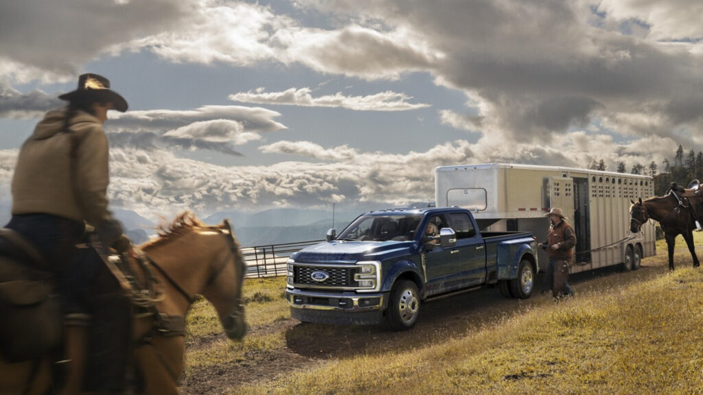 A man riding a horse next to a Ford F-450 Super Duty truck towing a horse trailer.