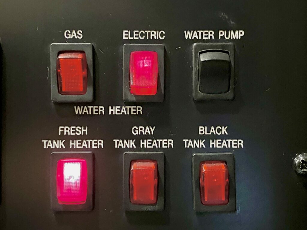 Close up shot of an RV control panel showing the three tank heater options for camping in cold weather. 