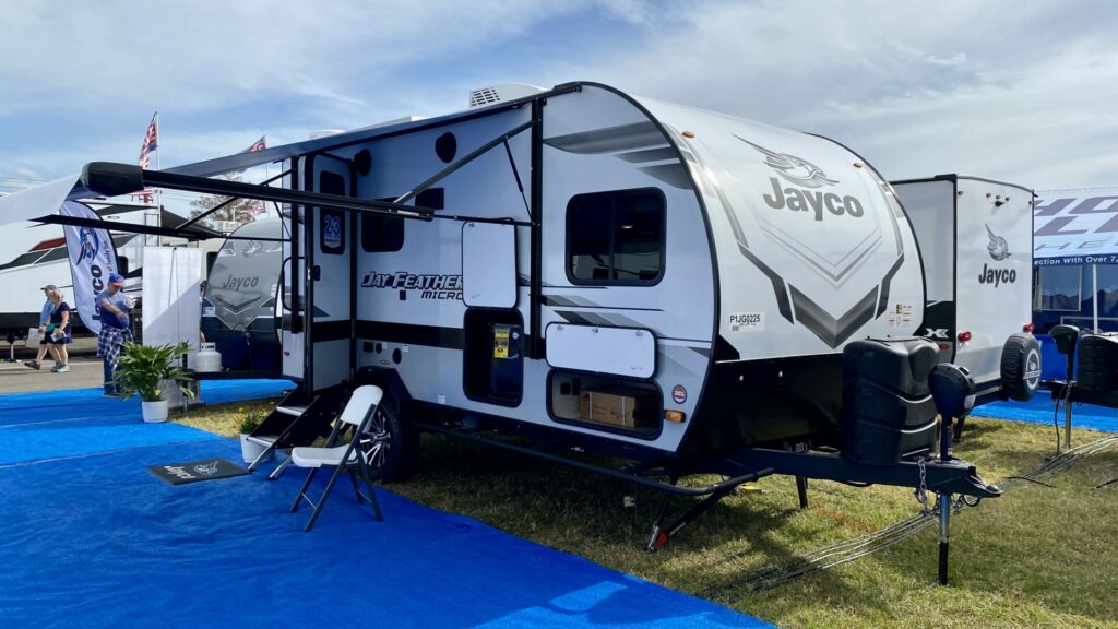 A Jayco travel trailer outside at an RV show with the door open and awning out 