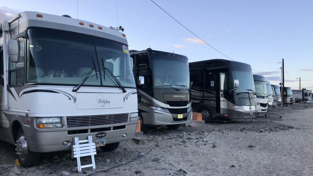 A row of used class A RVs parked on the beach. 