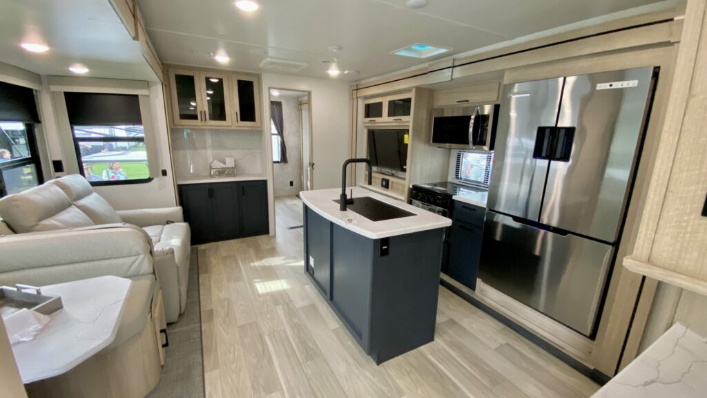 Interior shot of a travel trailer showing light interior colors with a dark accent color on the kitchen island. Modern interiors are something to consider when comparing used vs new RVs. 