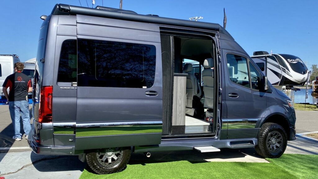 A Class B camper van at an RV show with the side door open 