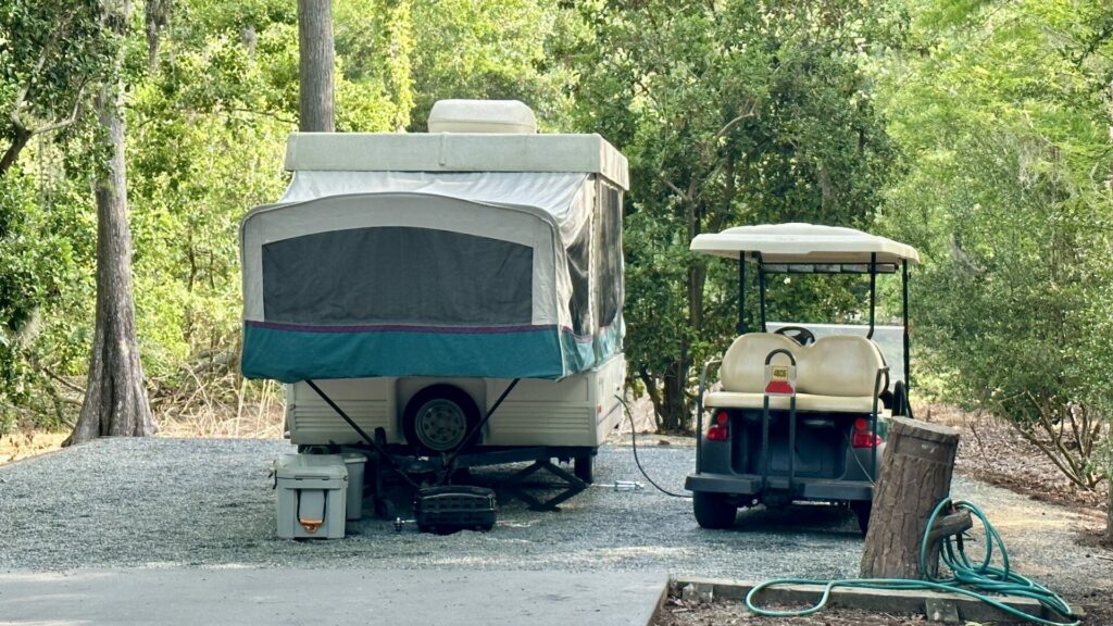 A pop up camper trailer setup in a campsite with a golf cart next to it