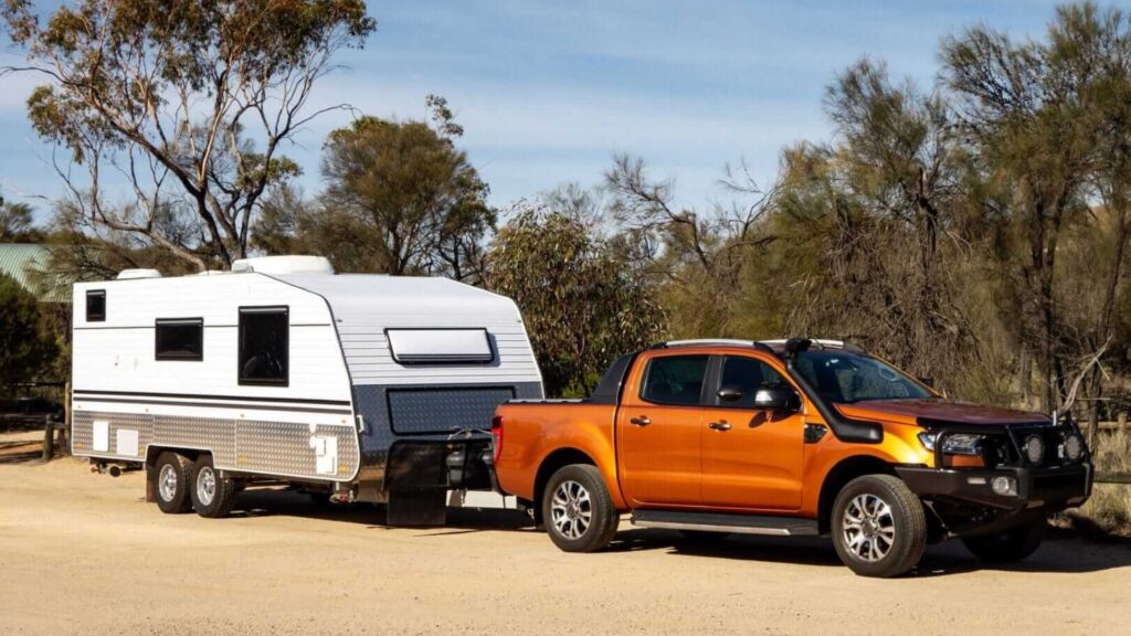An orange truck towing a travel trailer on a dirt road