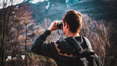 A man using binoculars in a national park to watch wildlife.