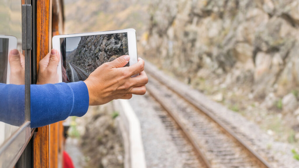 man sticking ipad camera out side of train