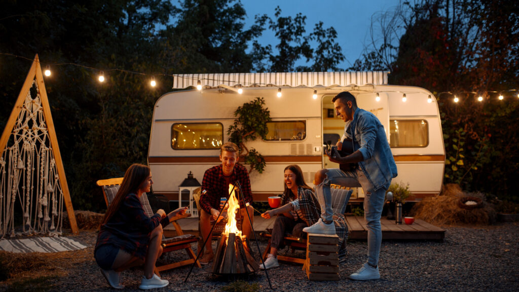 A group of friends singing around a campfire outside of their RV.