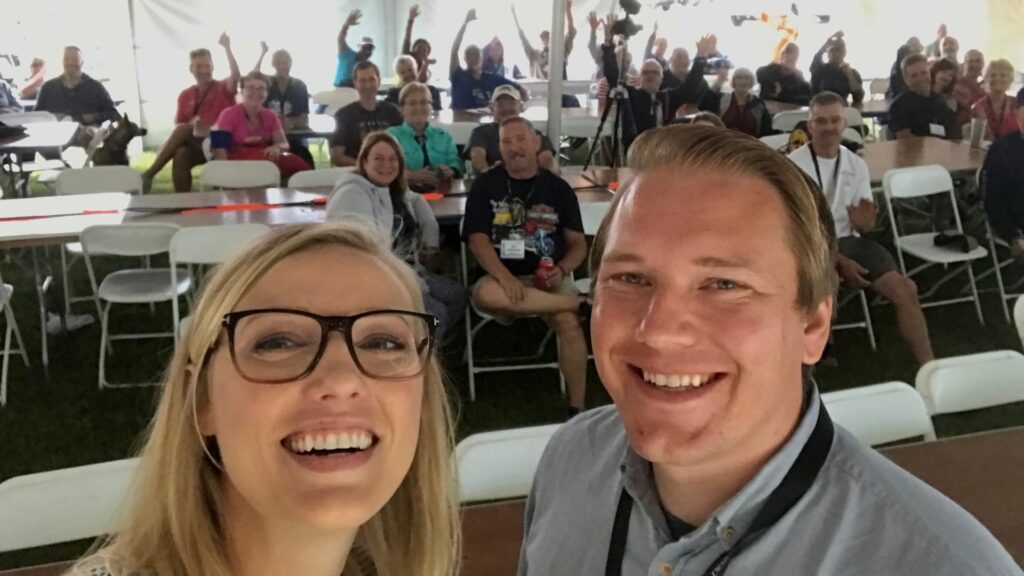 Rae and Jason taking a selfie in front of a crowd they just presented to