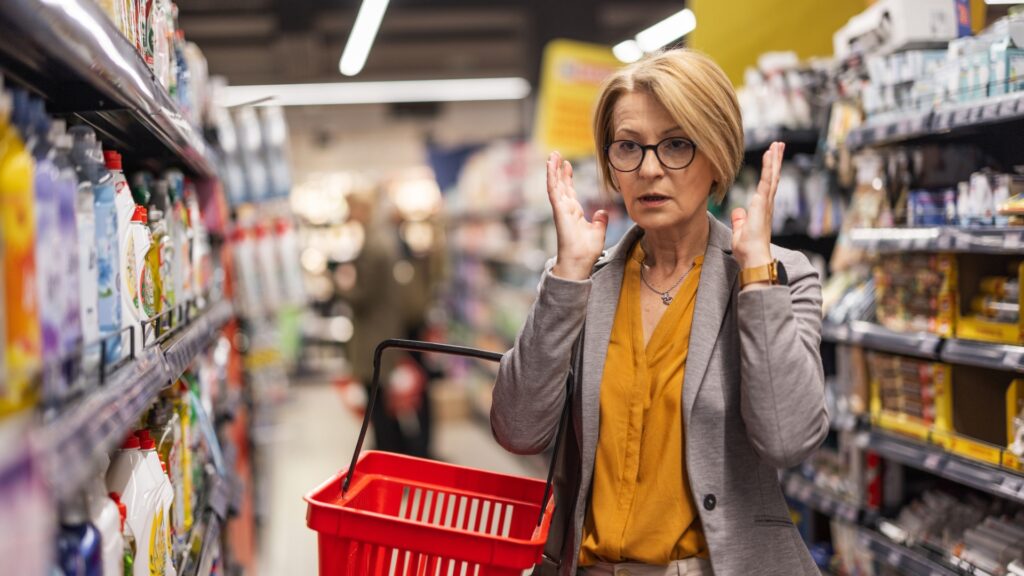A woman standing in a grocery store isle looking frustrated. 