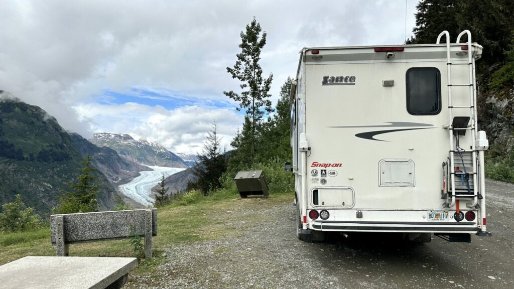 A truck camper parked on a dirt road in the pullout section overlooking a valley with a clear view of Salmon Glacier 