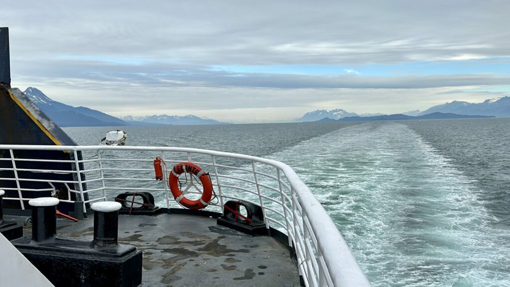 Our view on the alaska marine highway. A shot of the back of the ferry with the wake from it in the water and mountains in the background.