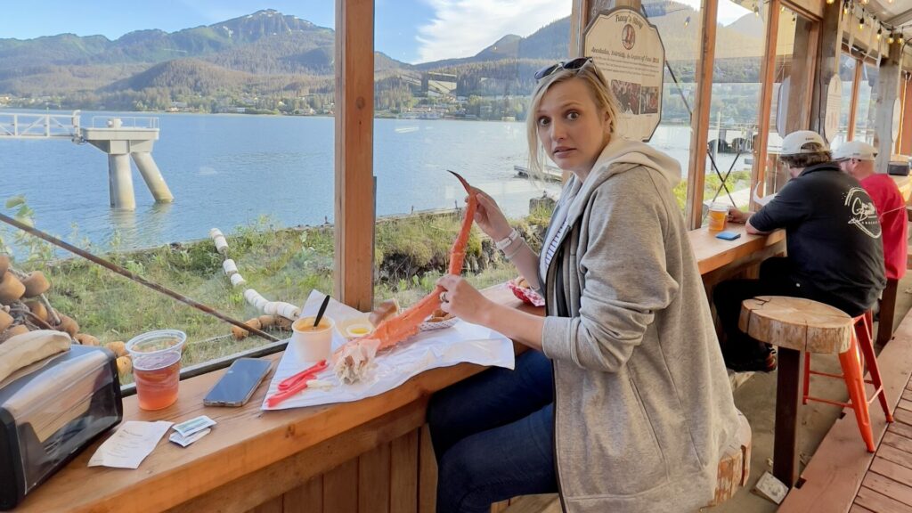 Rae eating a king crab leg in Juneau, Alaska. Hold it up to show how big it is with a shocked look on her face. 