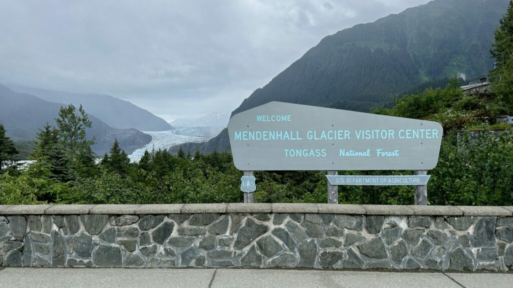A sign that says "Mendenhall Glacier Visitor Center" with the glacier in the background in Juneau, Alaska.  