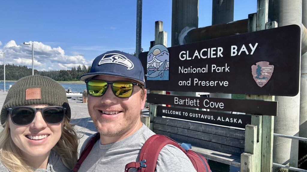 Rae and Jason standing in front of the Glacier Bay National Park and Preserve sign in Barlett Cove. 