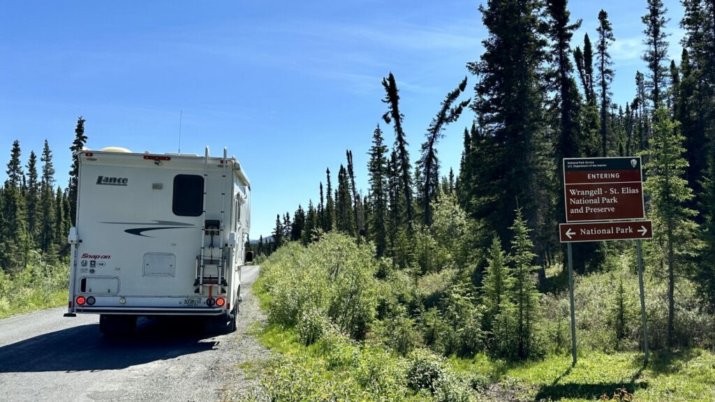 A truck camper parked on the side of a dirt road with the Entering Wrangell - St. Elias National Park and Preserve Sign 