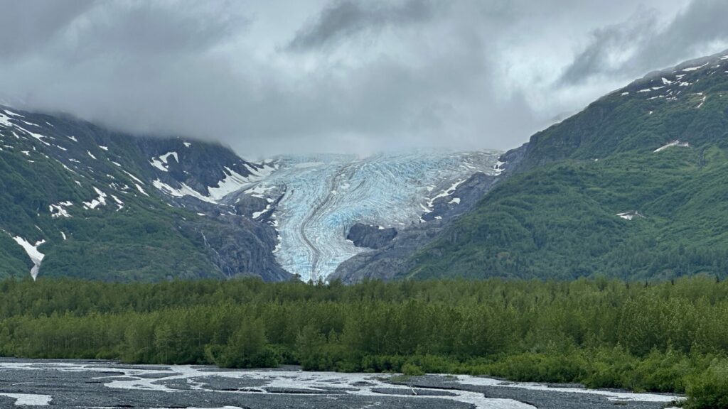 Exit Glacier peeking through the clouds with a green forest beneath it.