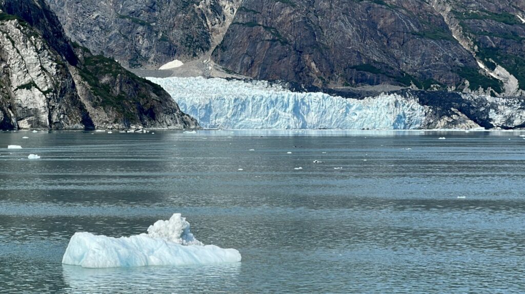 A glacier in the background with a chunk of ice floating in the foreground. 