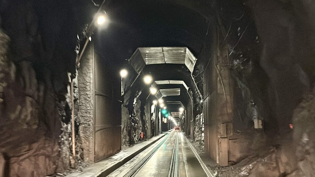 Inside the Whittier Tunnel showing the lights, exposed rock, and concrete panels. 