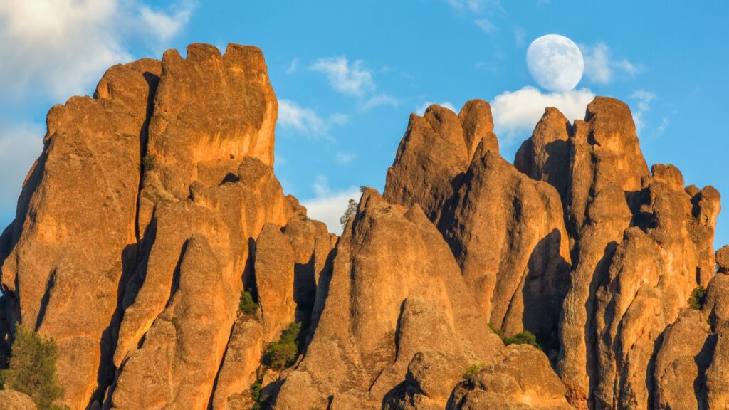 The moon rising over rock formations in pinnacles national park during the day. 
