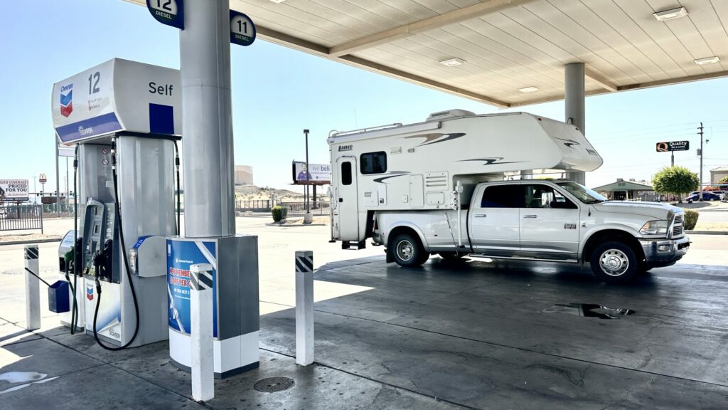 A truck camper parked at a gas station pump underneath the awning. 