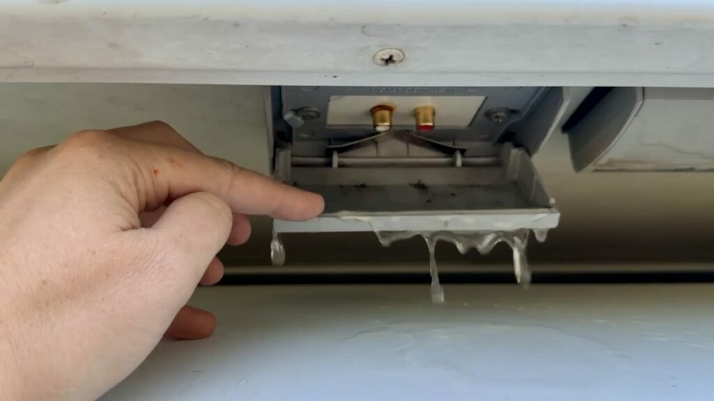 A hand holding open the cover for an exterior audio jack on a truck camper, with water dripping out.