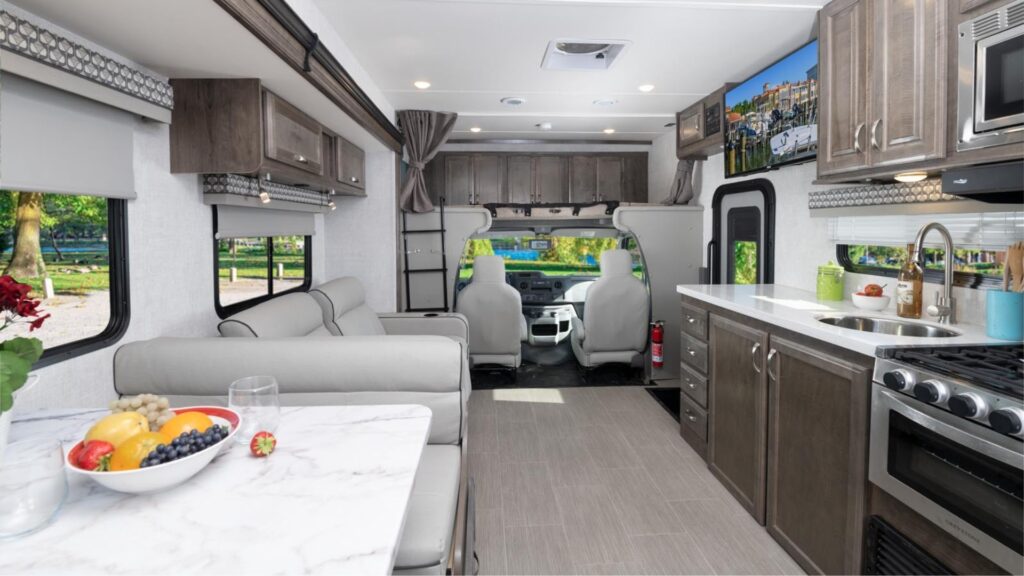 Interior shot of the Gulf Stream Conquest, one of the best small RVs. Shows the kichen area, driver's seat, and storage in the cab over area. 