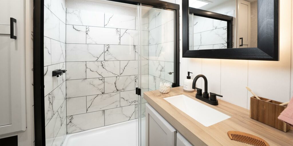 The bathroom of the Jayco Eagle 355MBQS with faux marble tile in the shower and black hardware.