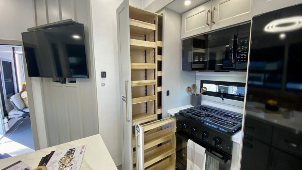 Interior shot of a toy hauler kitchen. It shows the cabinets open and pulled out to show the storage space. 