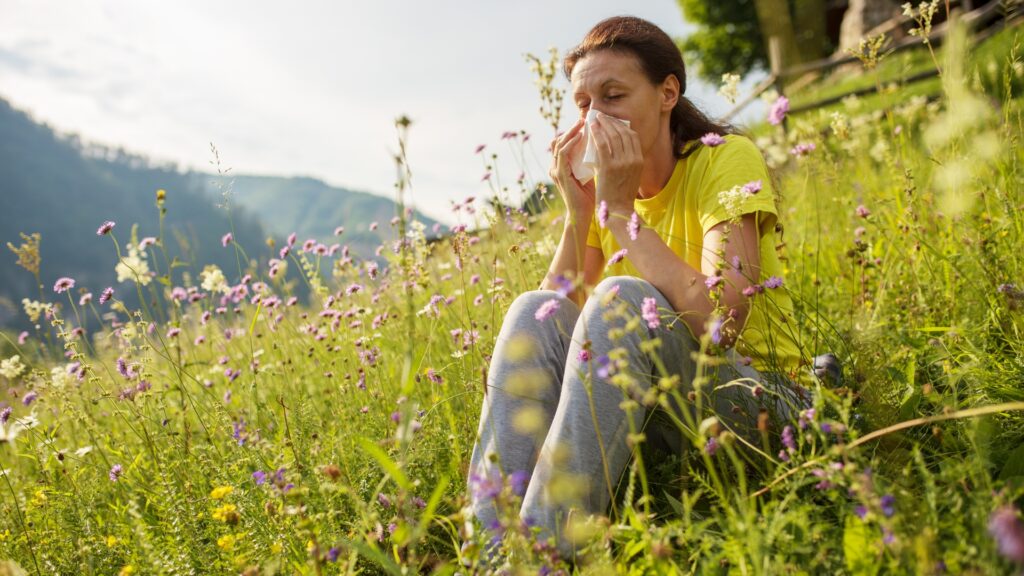 A woman in a field of flowers blowing her nose due to allergies. 