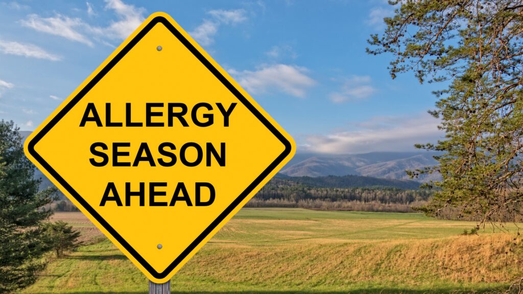a sign that says "allergy season ahead" with a grass field in the background.