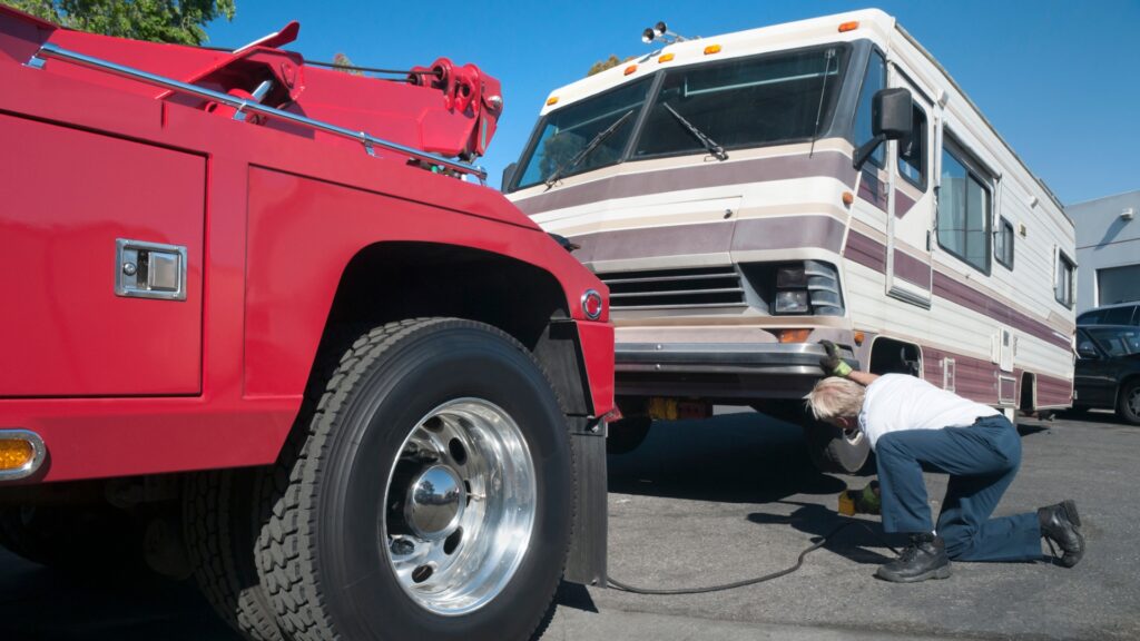 A man hooking up a tow truck to a broken down Class A RV.