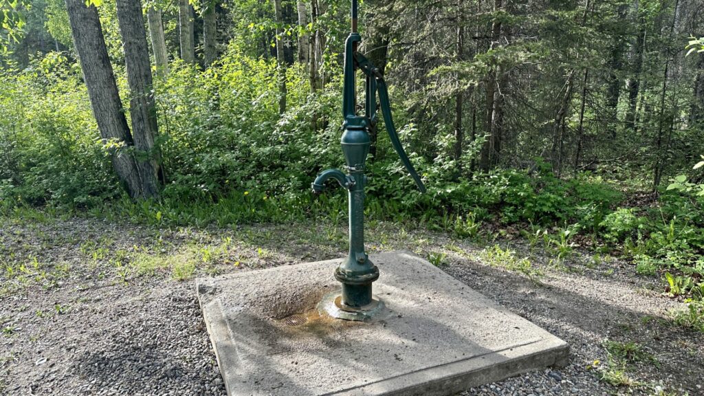 A pump that connects to well water and pumps out water when used. There is some rust on the ground.