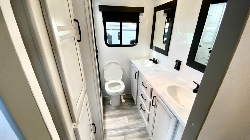 An RV bathroom with a toilet and double sinks and mirrors. 