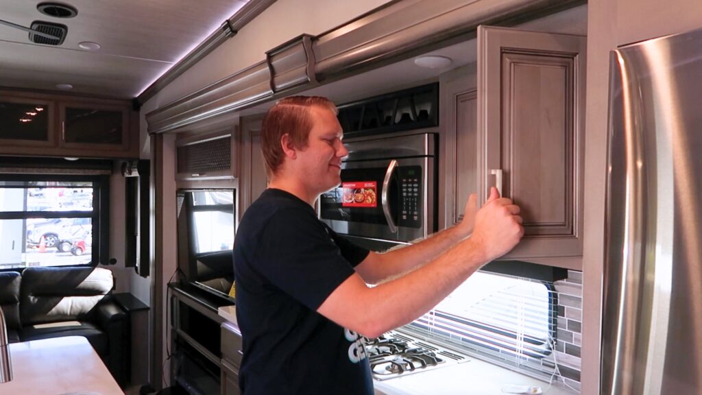 A man in an RV opening the cupboards with a smile on his face. He's testing everything in the RV floor plans he likes to make sure it is a good fit. 