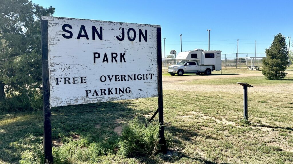 Our truck camper parked in a site with a sign in front that says "San Jon Park Free Overnight Parking"