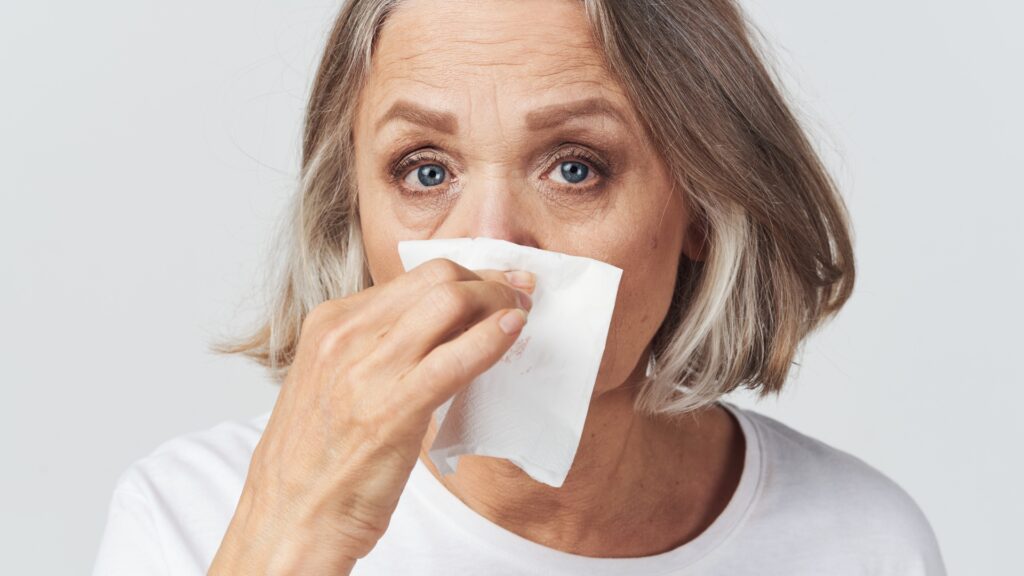 A woman looking at the camera holding a tissue to her nose. She has a stuffy nose after campfire.