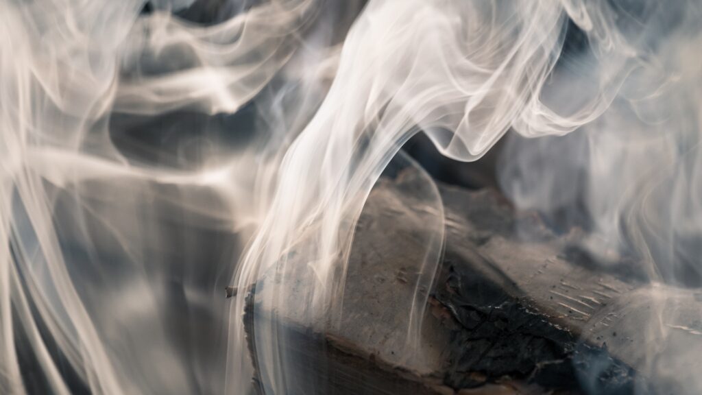 A close up shot of a log thats been burned with white smoke still billowing from it.