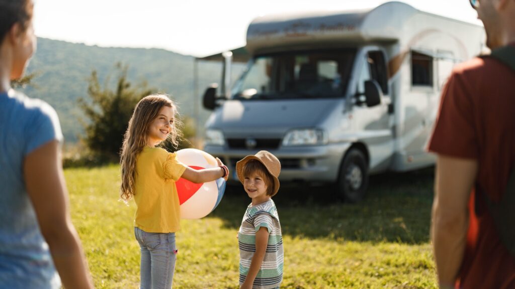 Kids smiling back at their parents with an RV in the background.