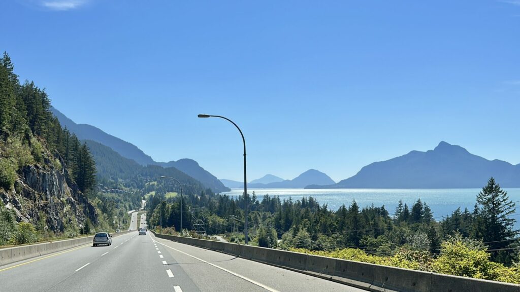 A view from the sea to sky highway showing the mountain terrain on the left and the stunning blue ocean water on the right. 